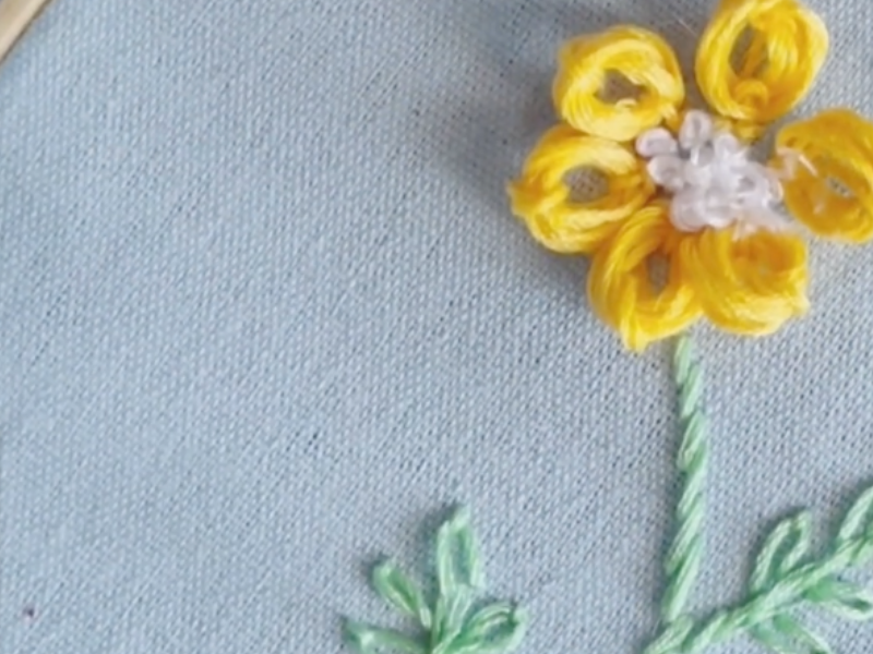 flor amarilla bordada en relieve con centro de nudo francés blanco y tallo verde